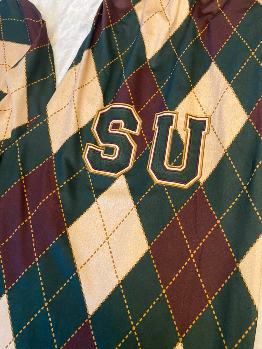 Close-up of SU lettering on burgundy forest green and cream argyle pajama fabric